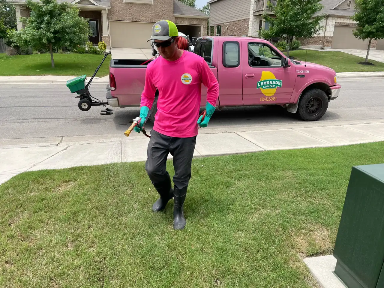 Lemonade Lawn Care technician spraying weed control beside pink branded pickup truck