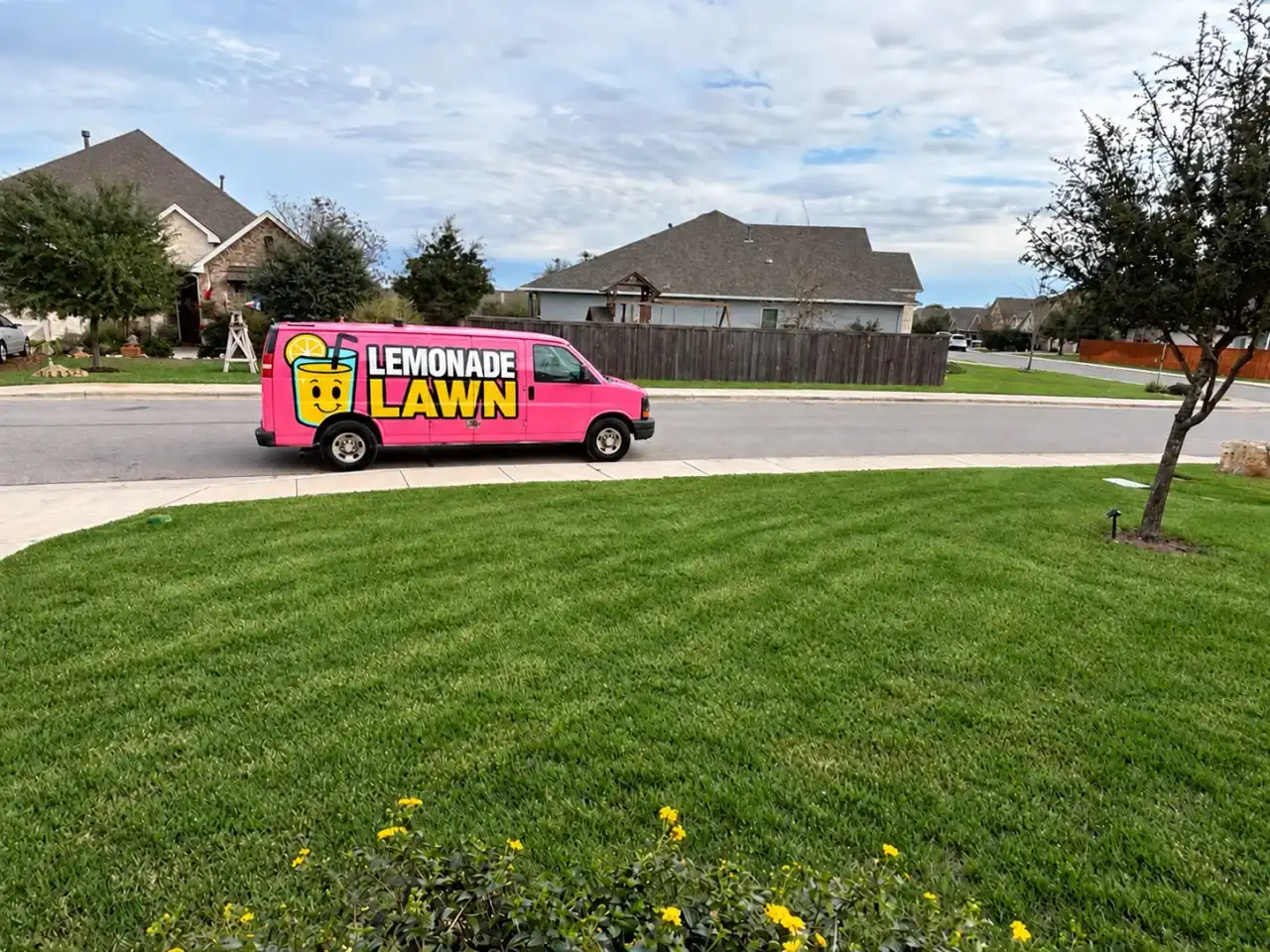 Pink Lemonade Lawn Care van parked on a New Braunfels street in front of a thick green Bermuda lawn